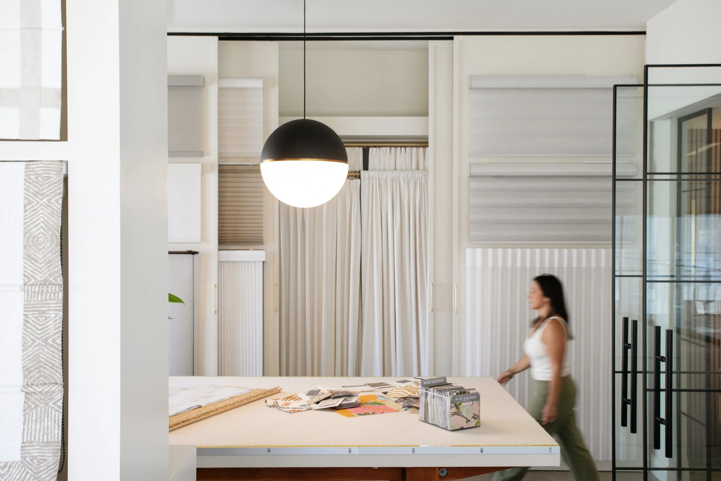 Showroom interior with drapery, roman shade, and blind displays around a fabric worktable, Santa Rosa, by AVCO Design