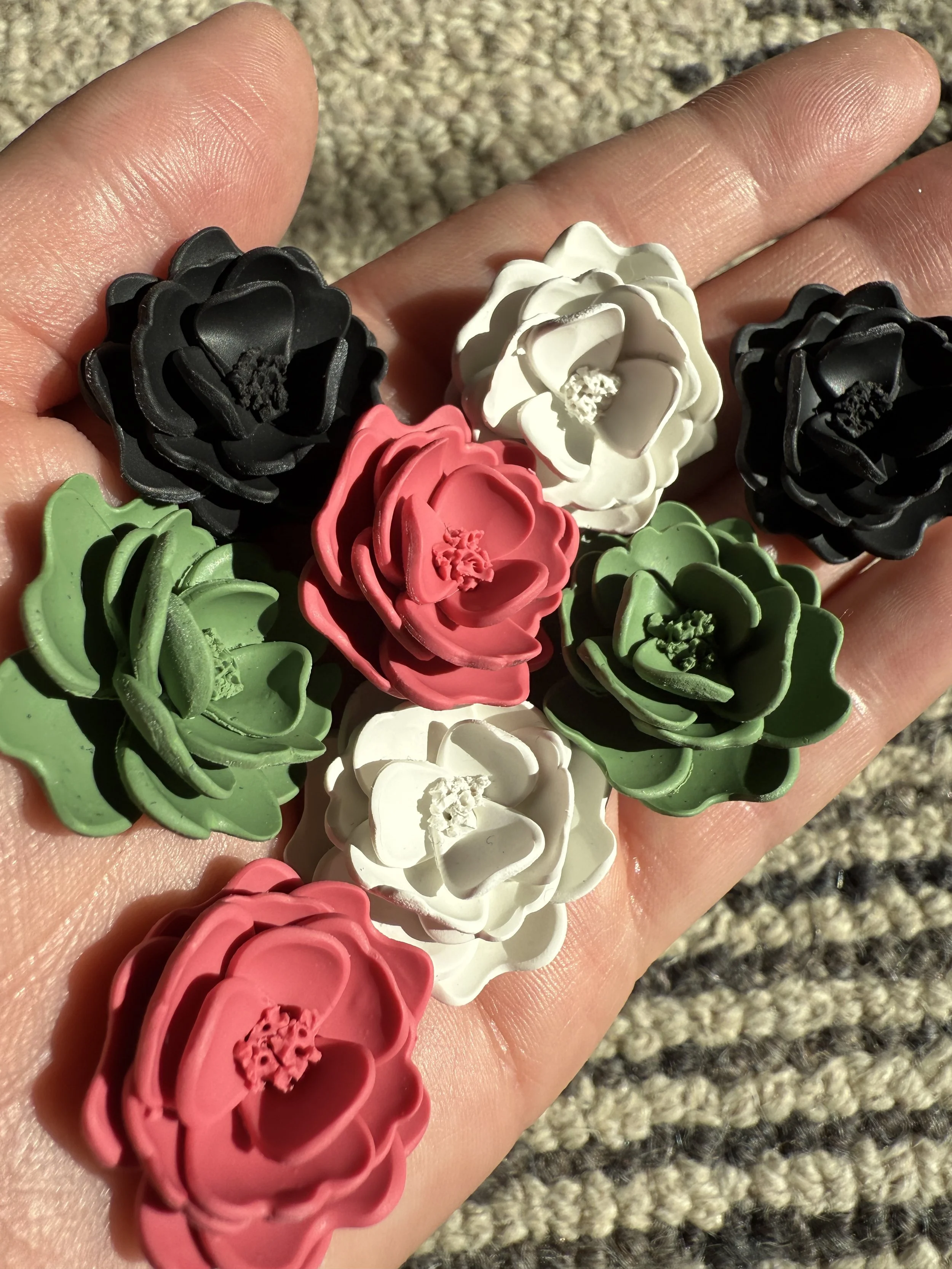 Colorful flowers in black, white, pink, and green, arranged on a person's hand outdoors, with sunlight casting shadows.