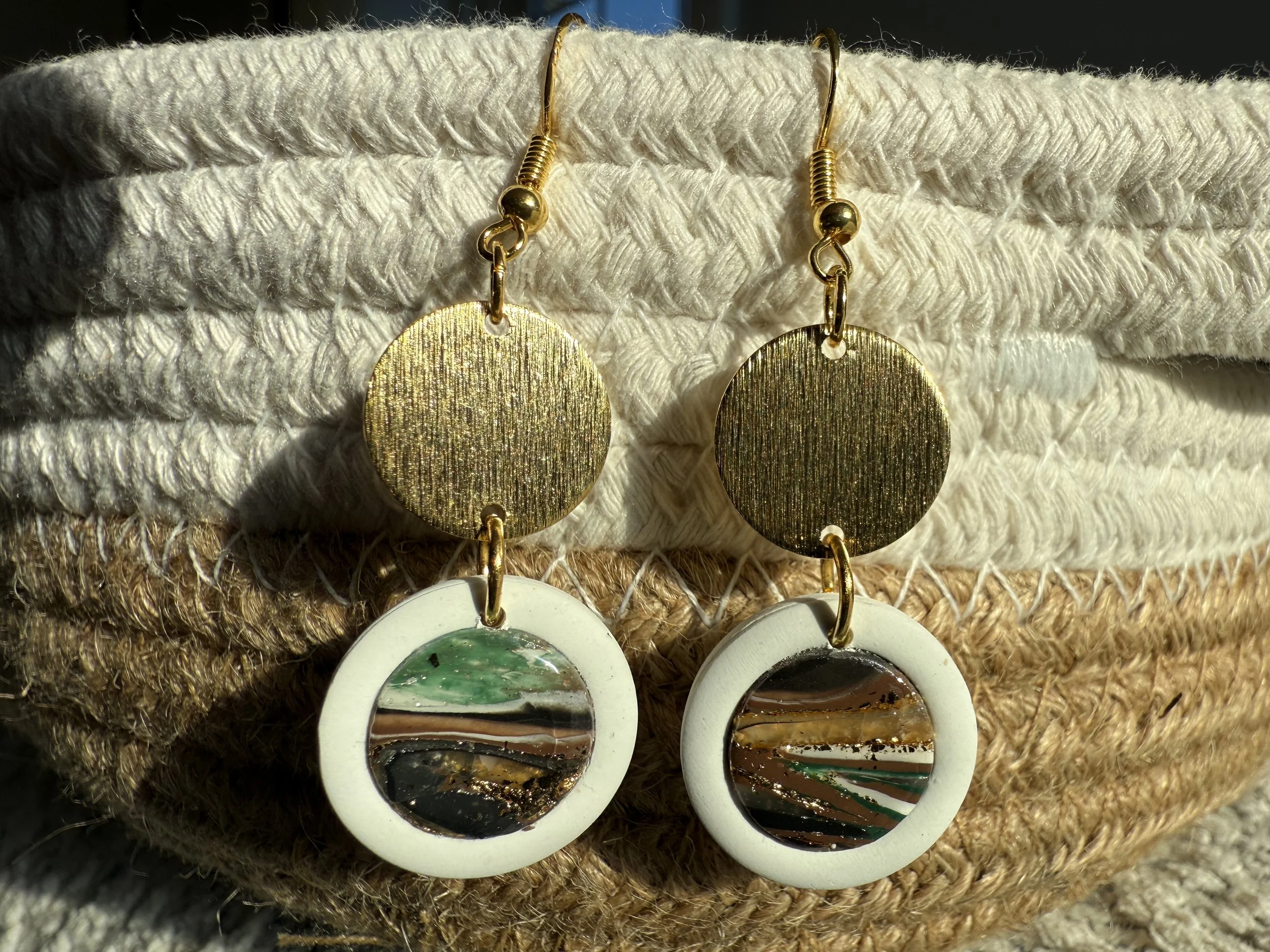 Gold and multicolored round earrings hanging on a textured fabric surface.