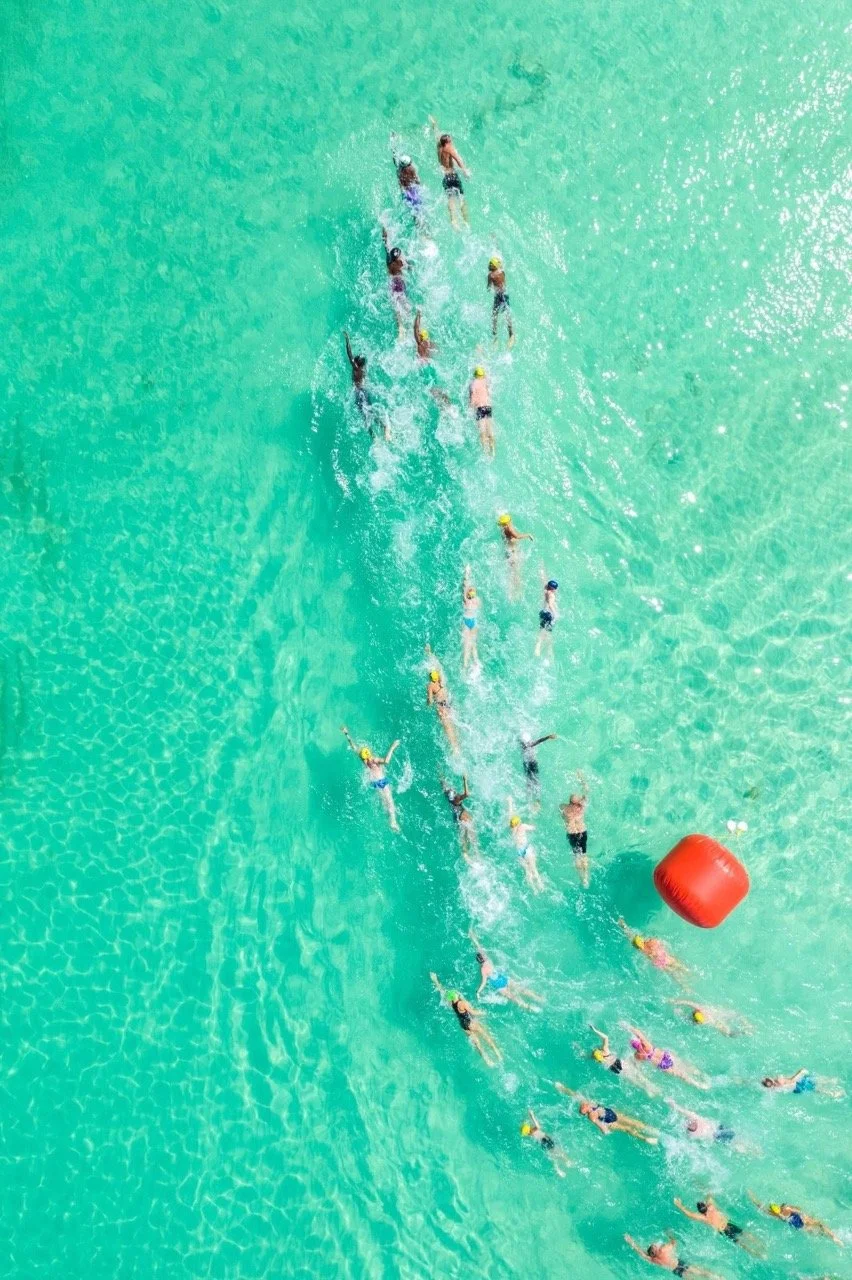 Aerial view of a swim race in turquoise ocean water of Grace Bay Beach with a red buoy floating nearby.