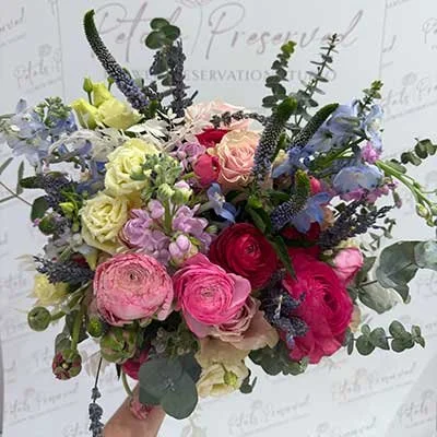 A colorful bouquet of various flowers including roses, lisianthus, and lavender with green foliage against a white background.