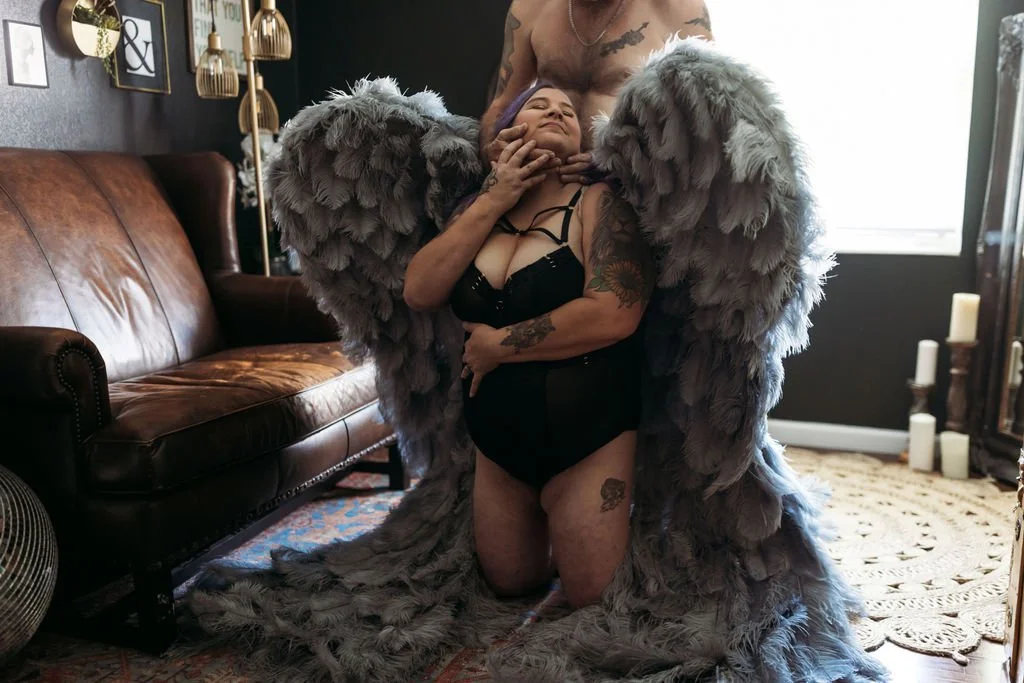 Woman sitting with gray angel wings while embracing her husband during their boudoir session