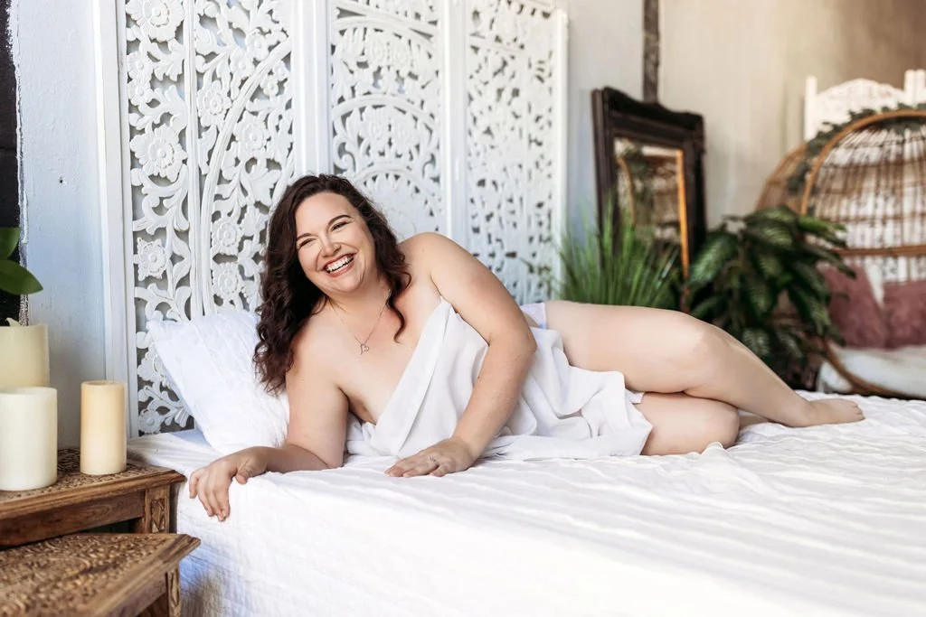 Woman laughing while lying on a bed during her solo boudoir portraits in Jacksonville