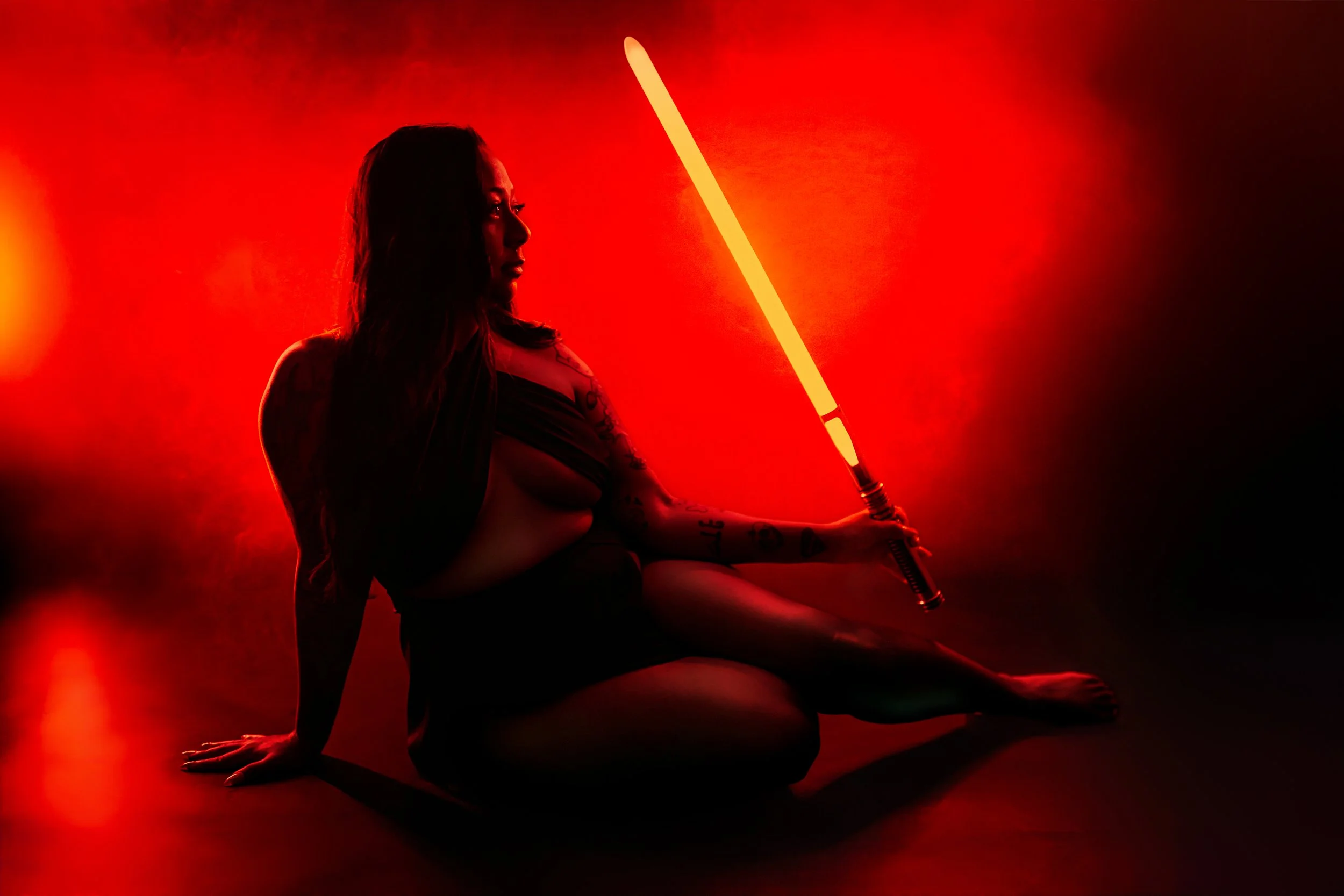 Woman posing with a glowing red lightsaber during a creative boudoir session at Hype Girl Boudoir