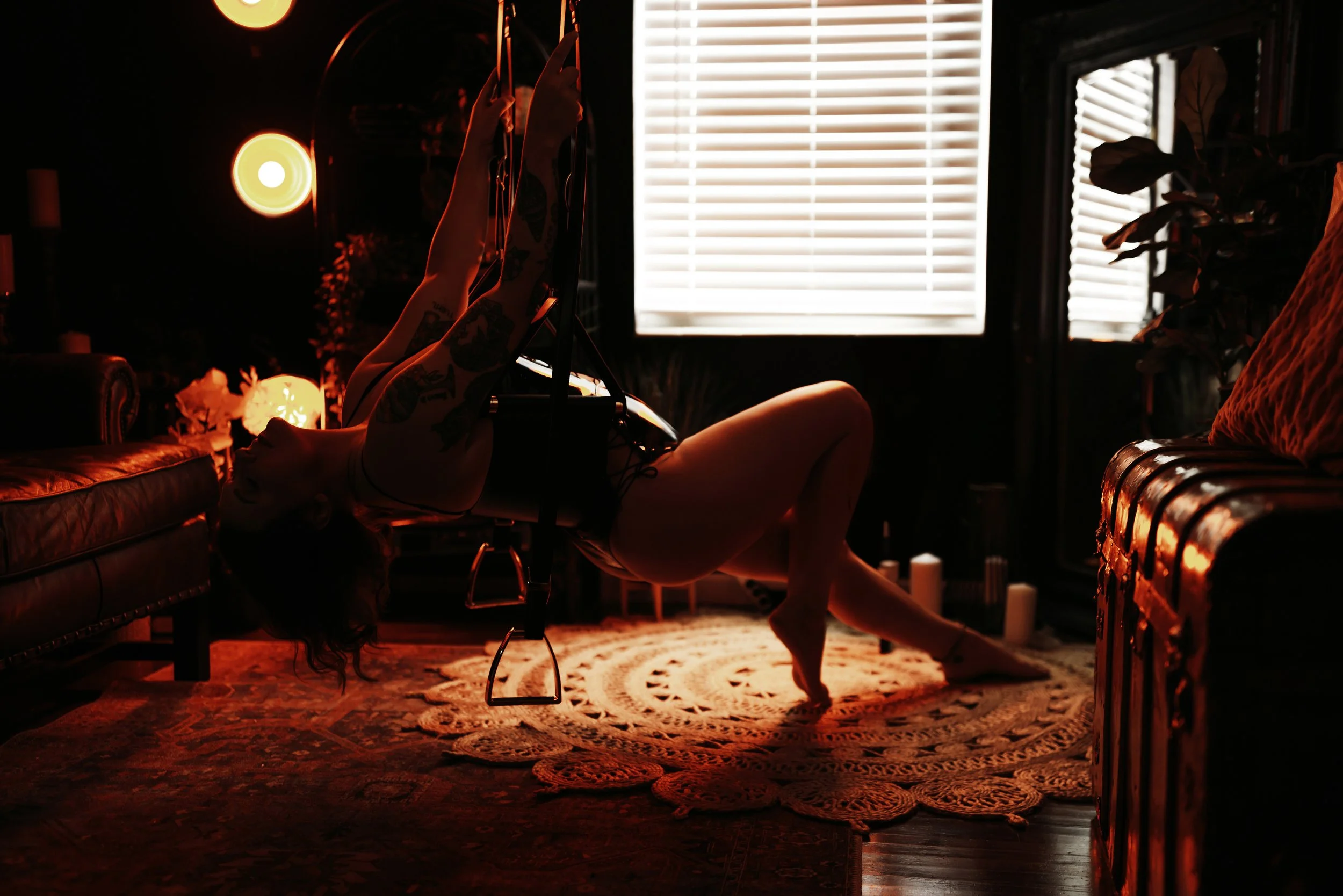 Woman posing in a swing in a red-lit studio set.