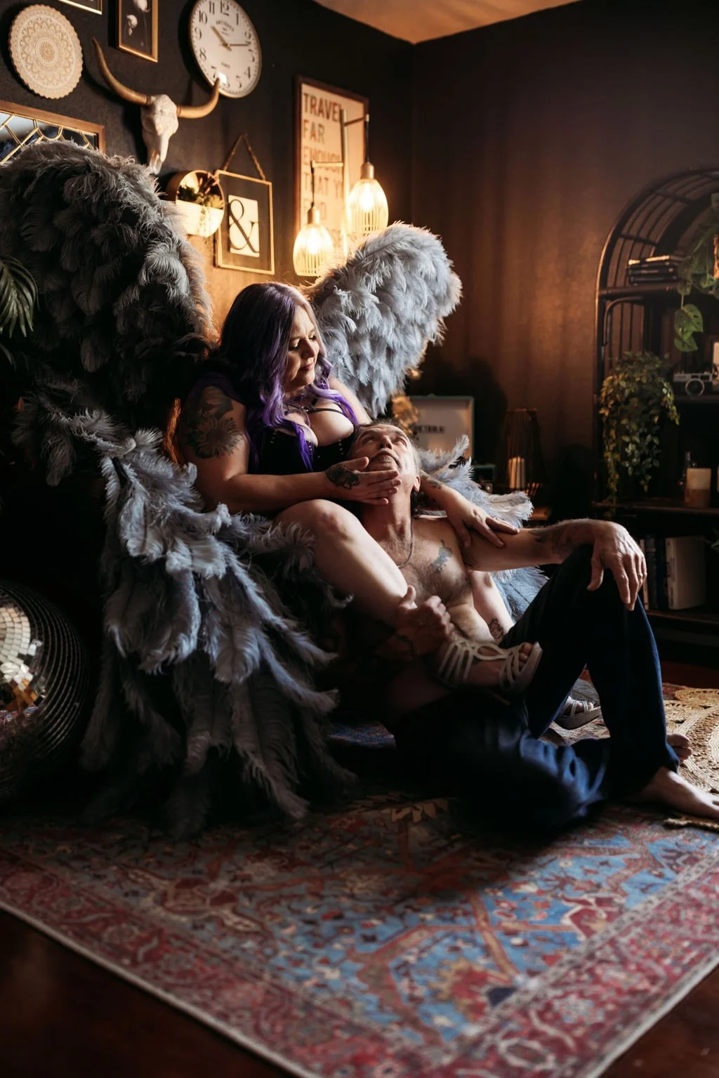 Tattooed couple posing together with dramatic gray angel wings in the boudoir studio