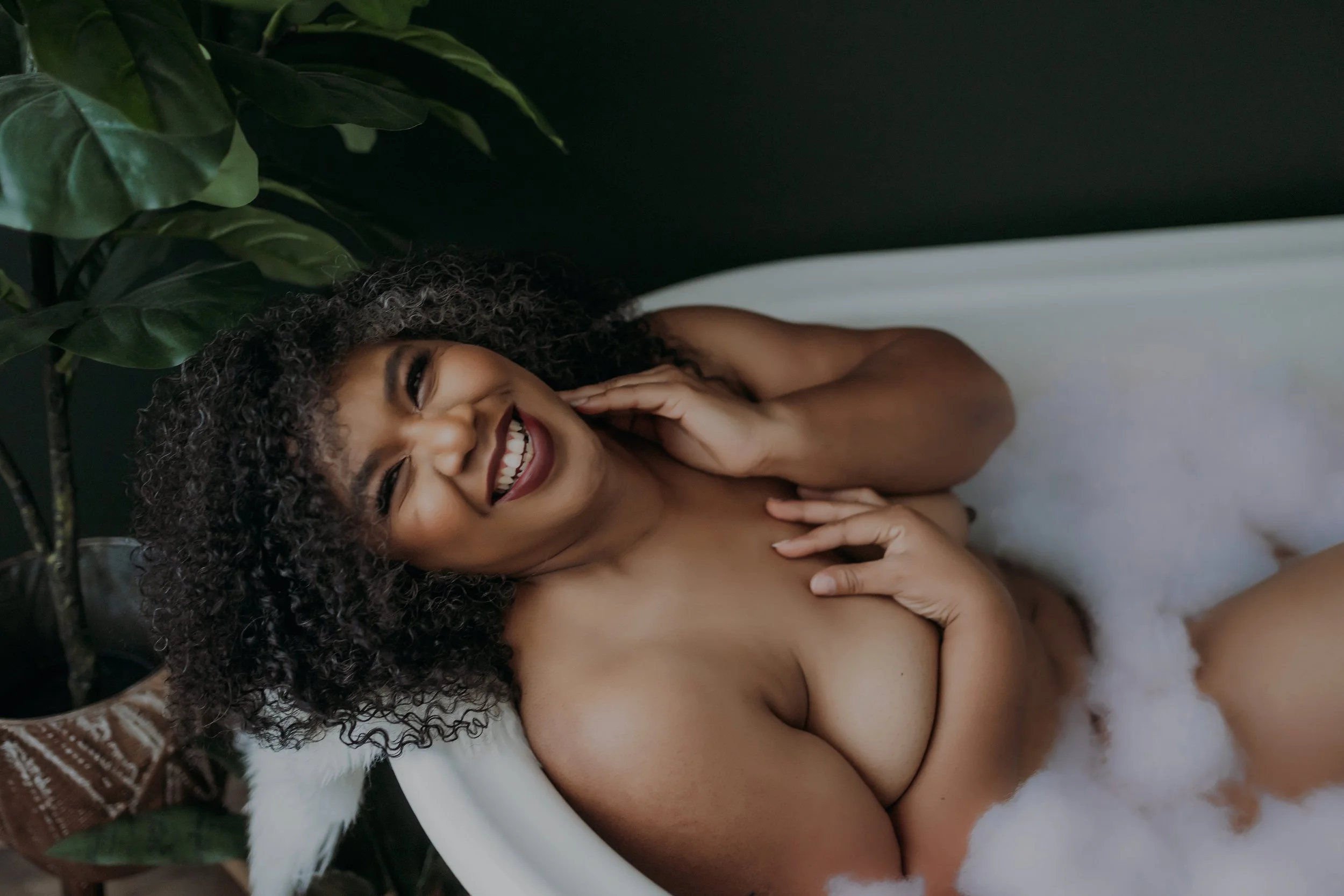 Smiling woman relaxing in a bubble bath during her boudoir session in Jacksonville, Florida