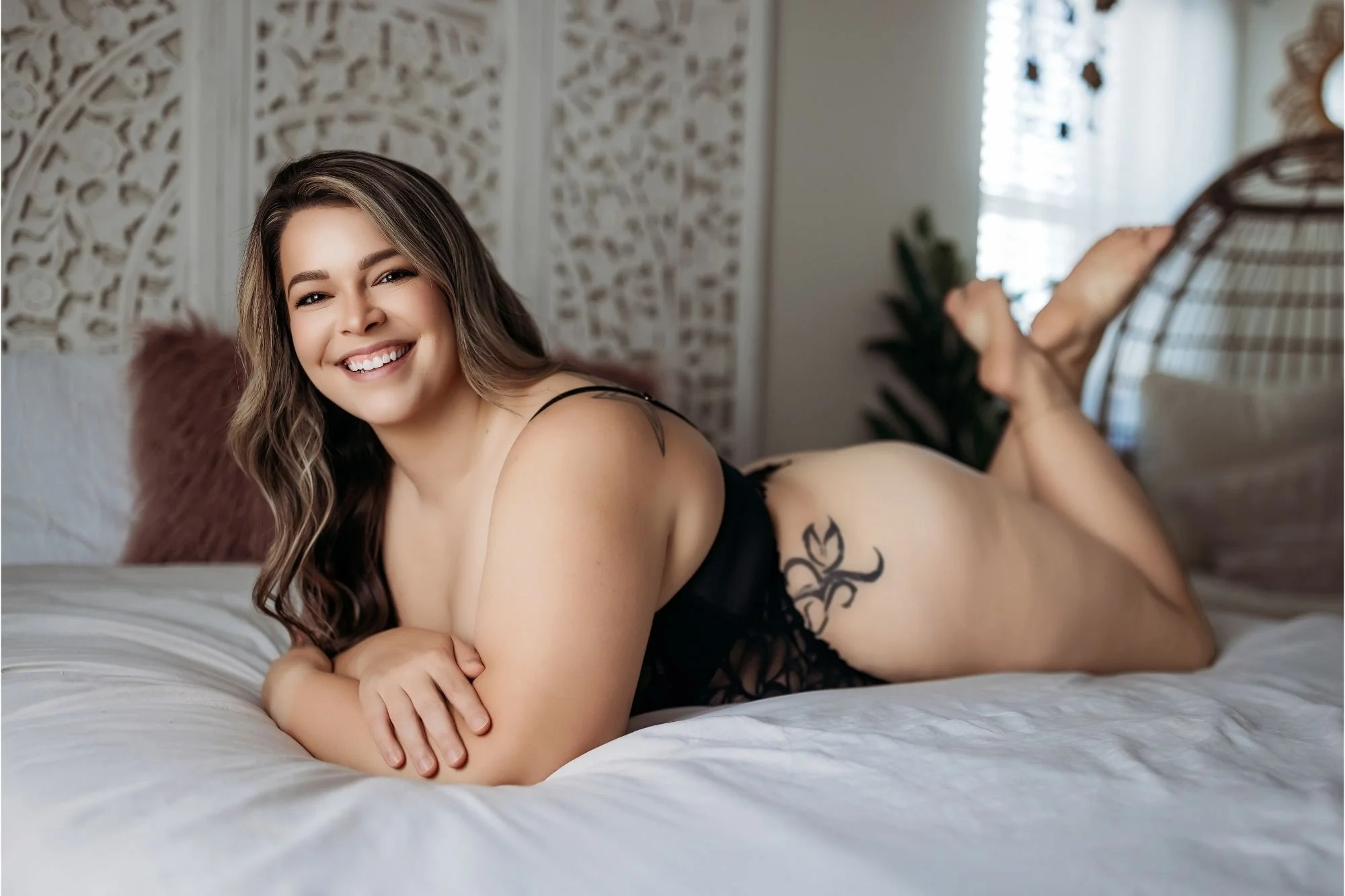 Smiling woman lying on a white bed in black lingerie with her feet raised behind her.