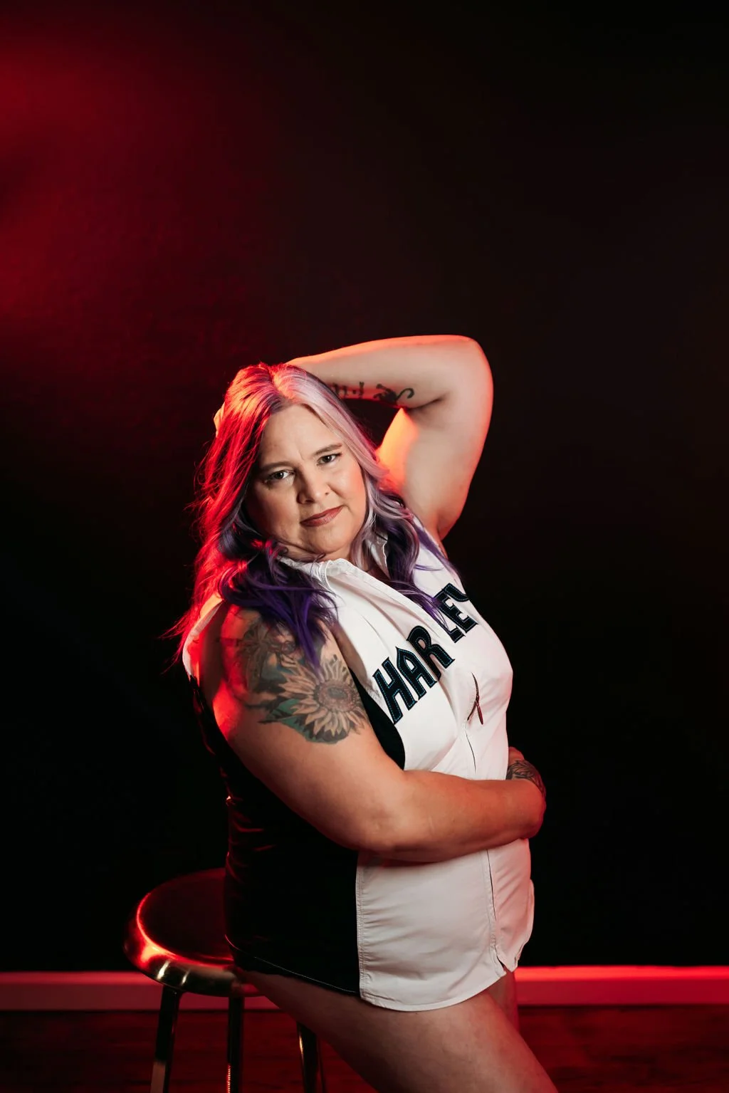 Woman posing in a Harley Davidson top under dramatic red lighting during her boudoir session