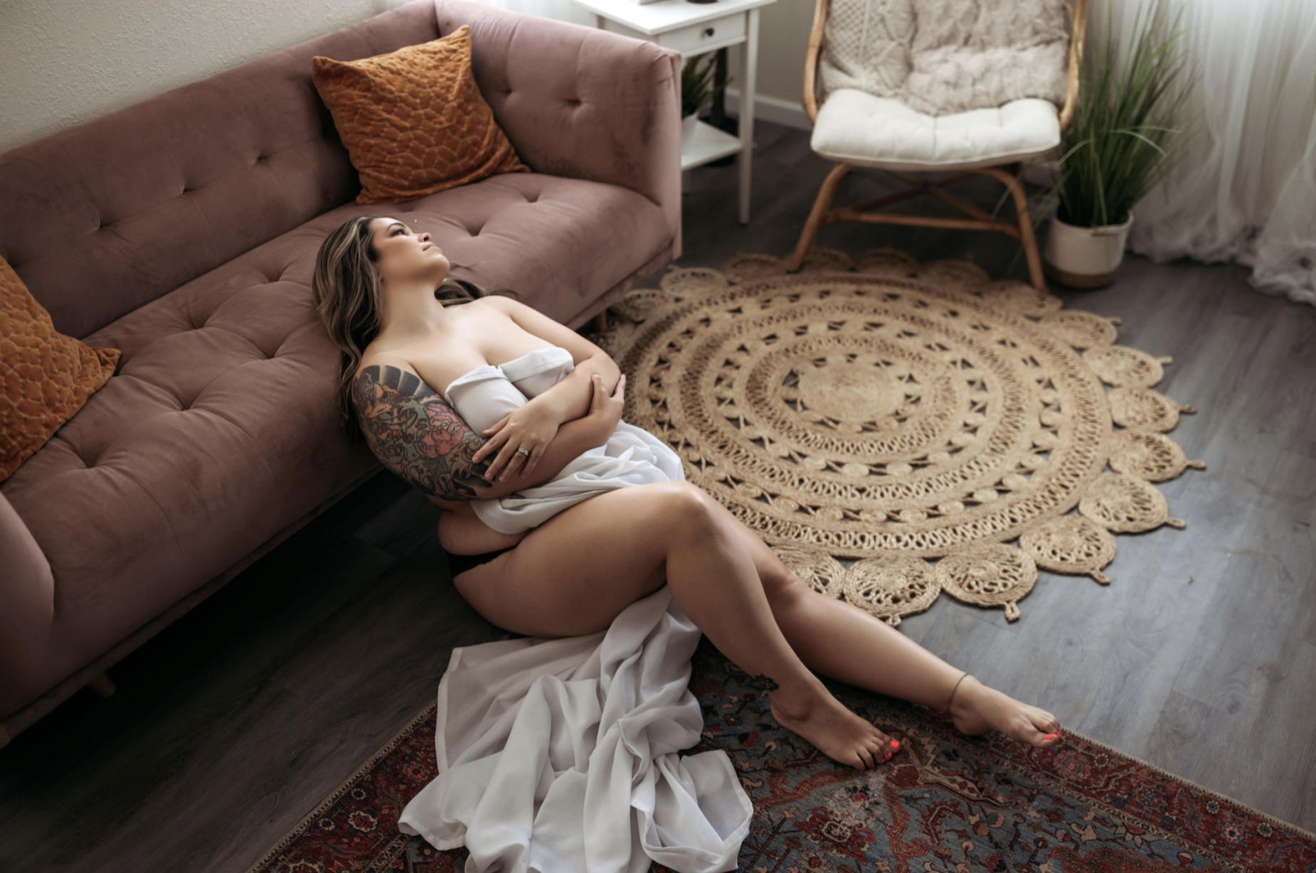 Woman wrapped in a white sheet leaning against a mauve sofa.
