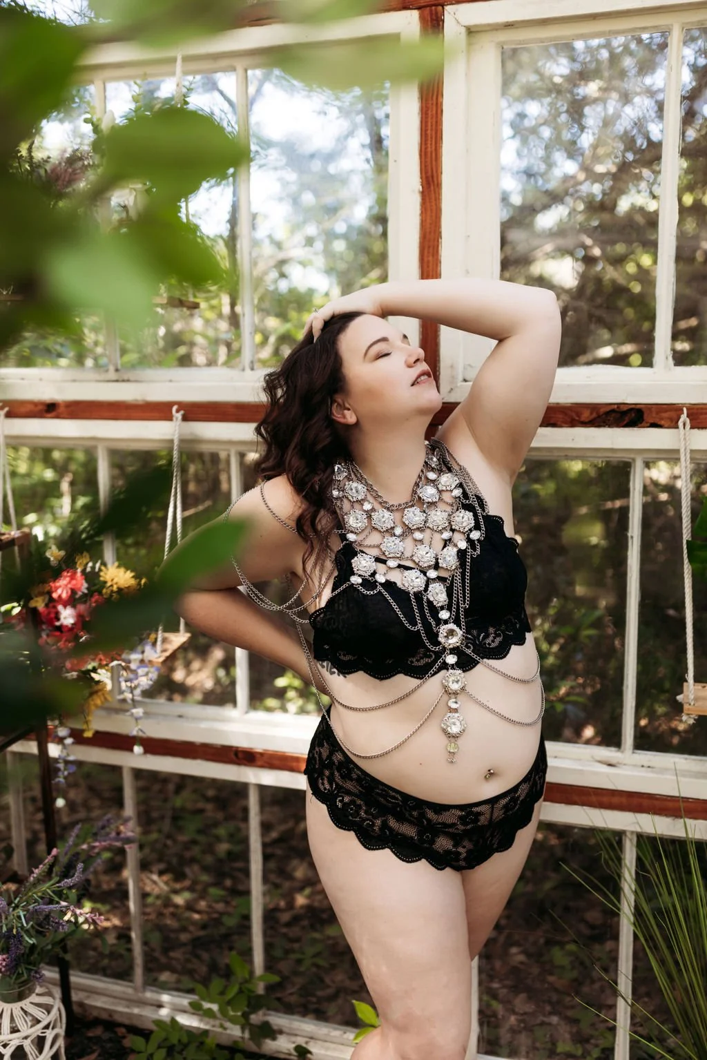 Woman posing in black lingerie and statement body jewelry inside a greenhouse