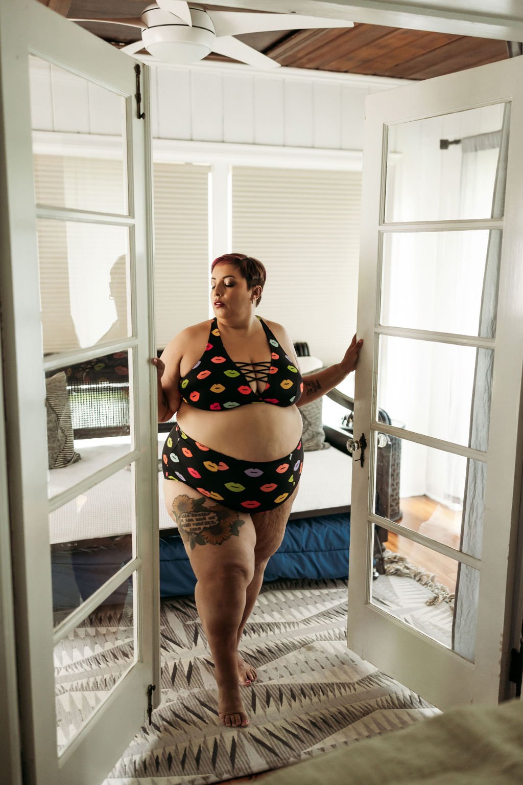 Plus-size woman in colorful kiss-print lingerie posing between French doors during her boudoir session