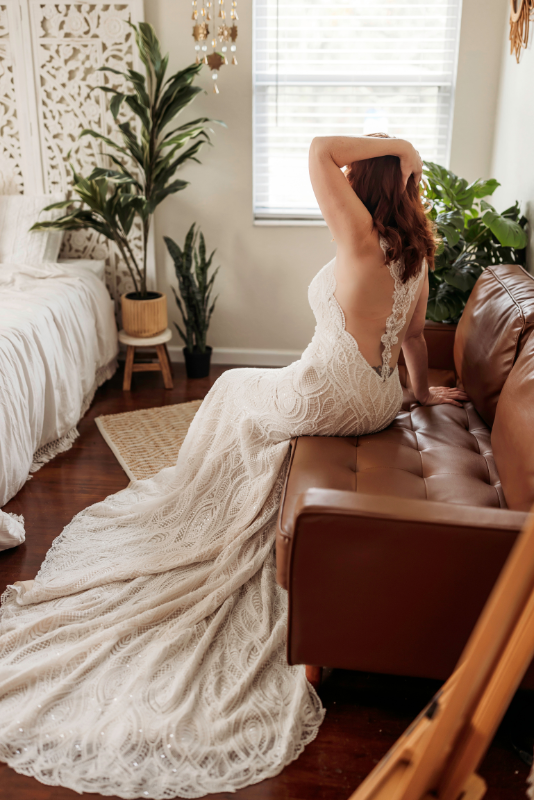 Woman in a white lace gown seated on a brown sofa.
