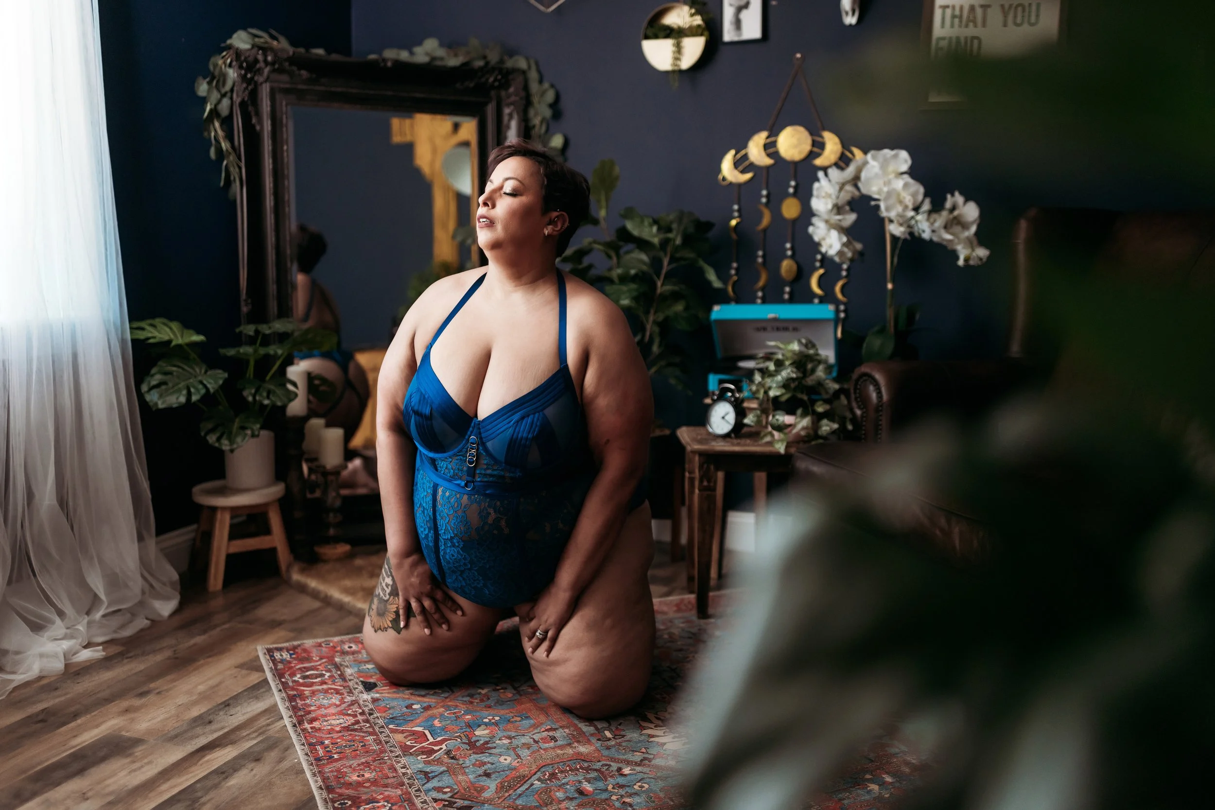 Plus-size woman kneeling in a blue lace bodysuit during a boudoir session in Jacksonville, Florida