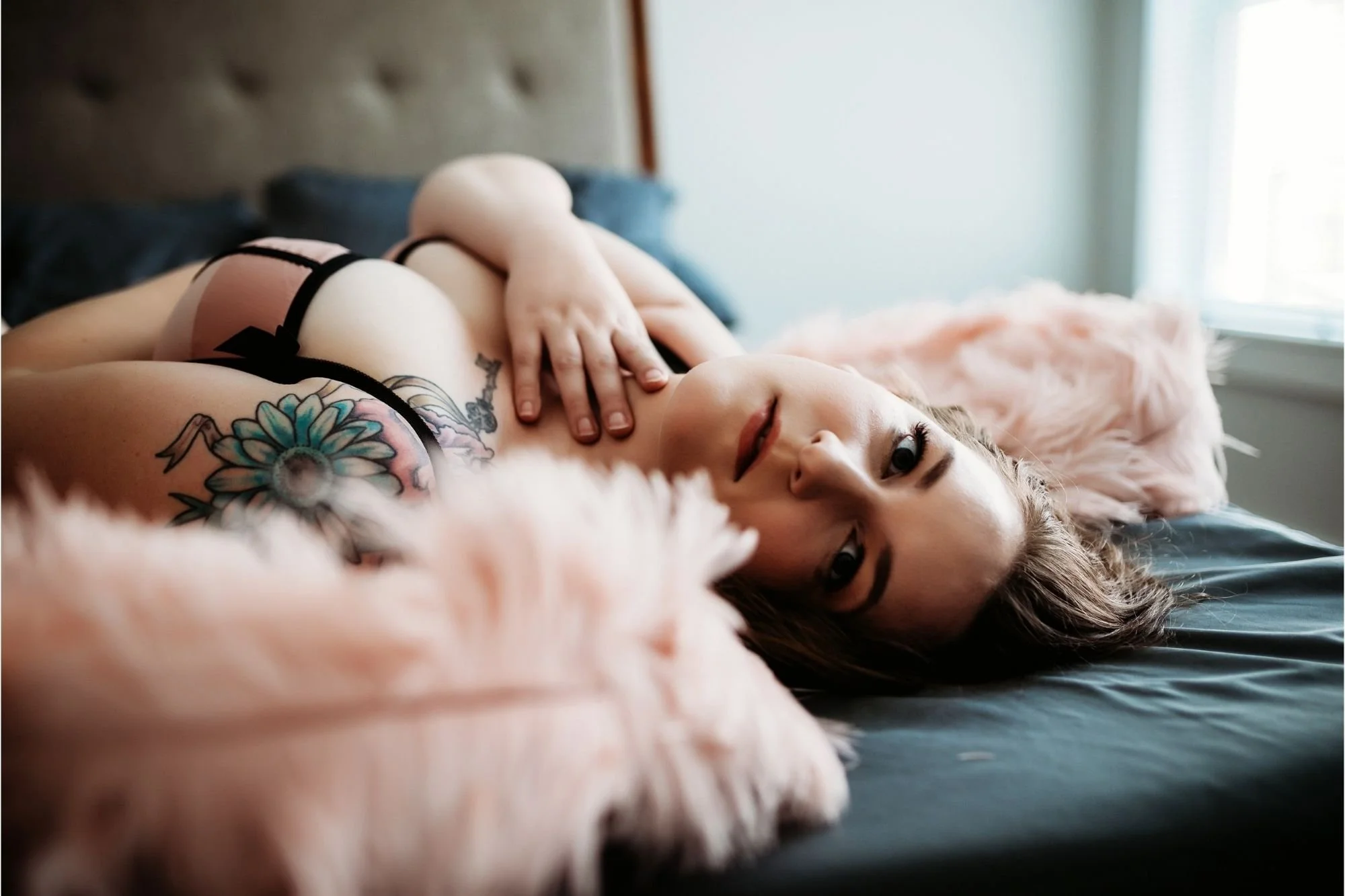 Woman reclining on a bed with pink feathers around her shoulders.