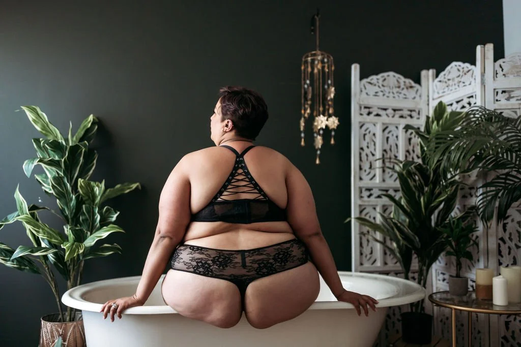 Plus-size woman in black lace lingerie posing on the edge of a clawfoot tub during a Jacksonville boudoir session