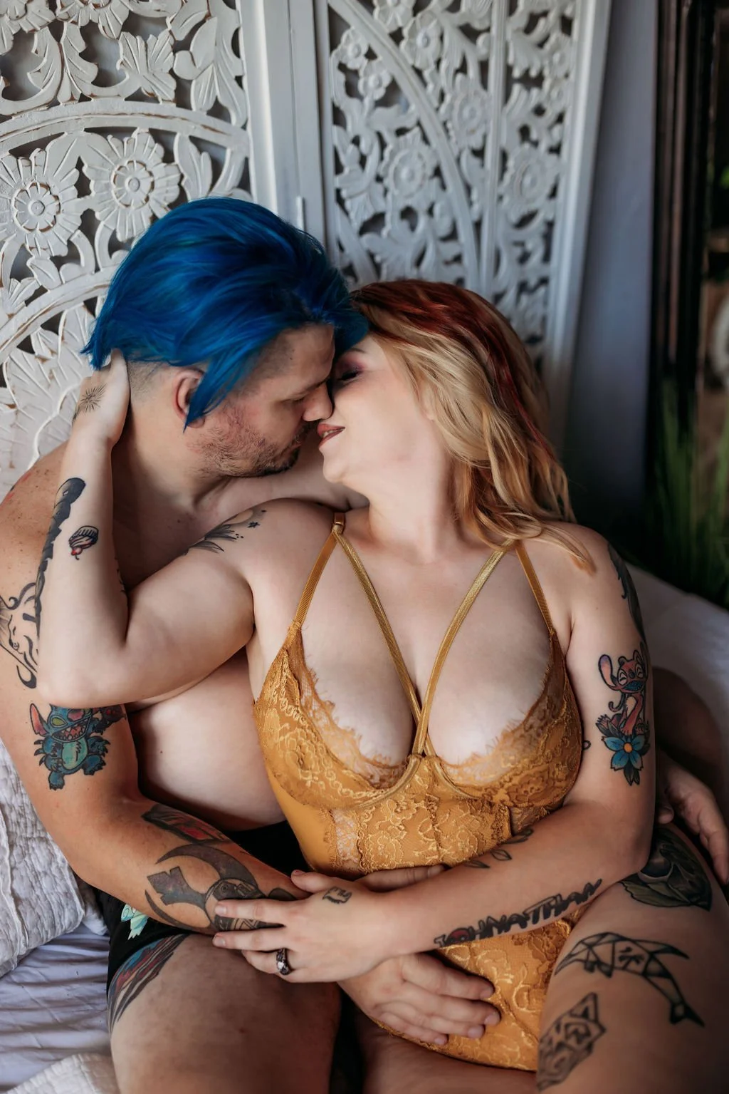 Tattooed couple leaning in for a kiss while sitting together on a bed