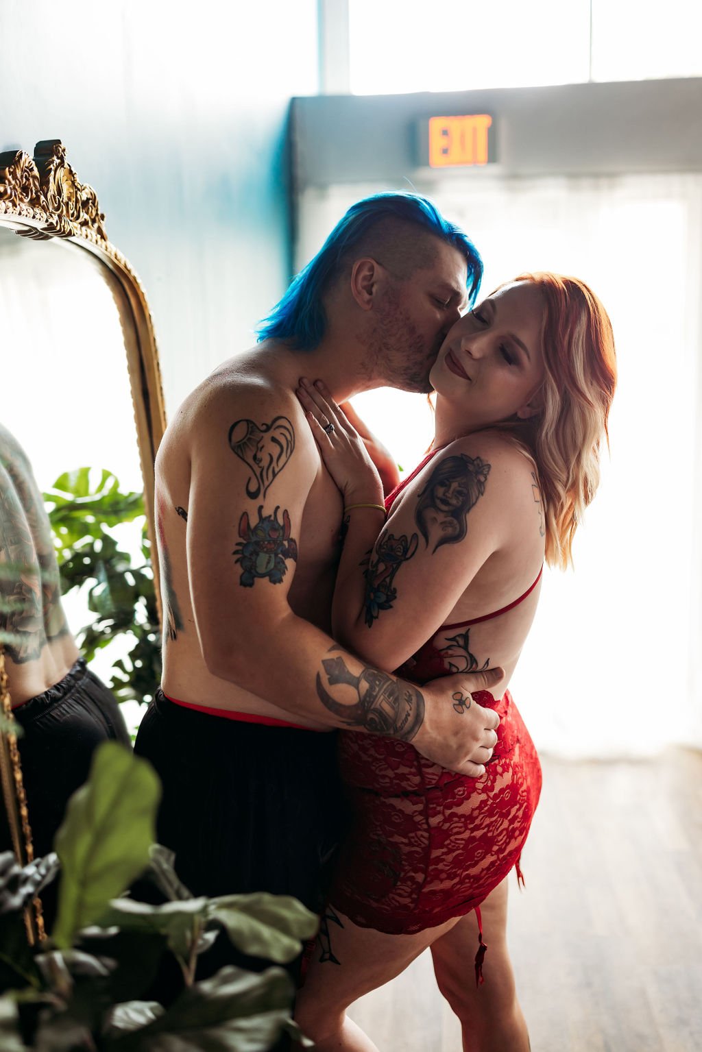 Tattooed couple posing together in front of a mirror during a spicy couples boudoir session