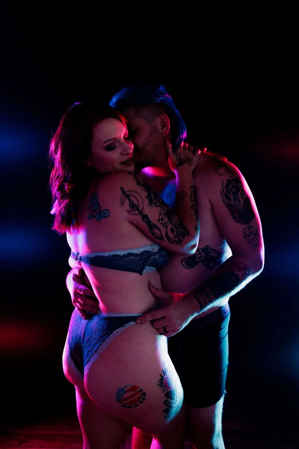 Tattooed couple posing closely together under pink and blue neon lighting