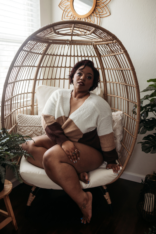 Woman in a white cardigan and black bottoms sitting in a wicker chair.