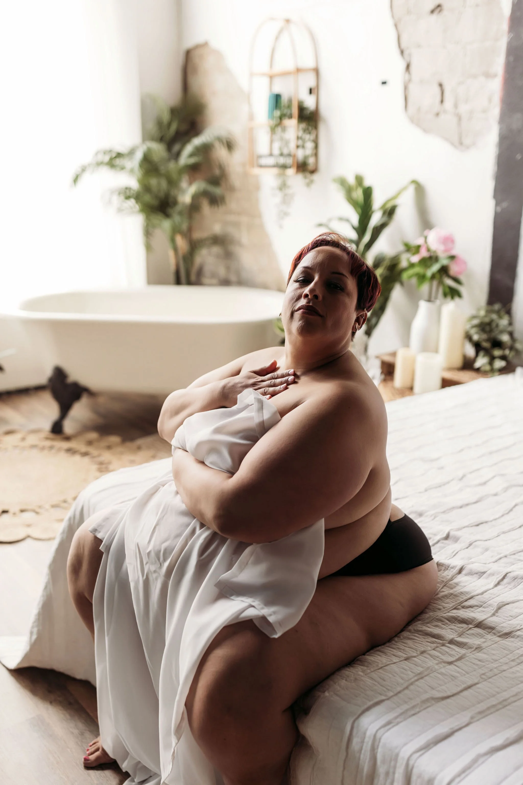 Woman wrapped in a white sheet posing on a bed during a Jacksonville boudoir photography session