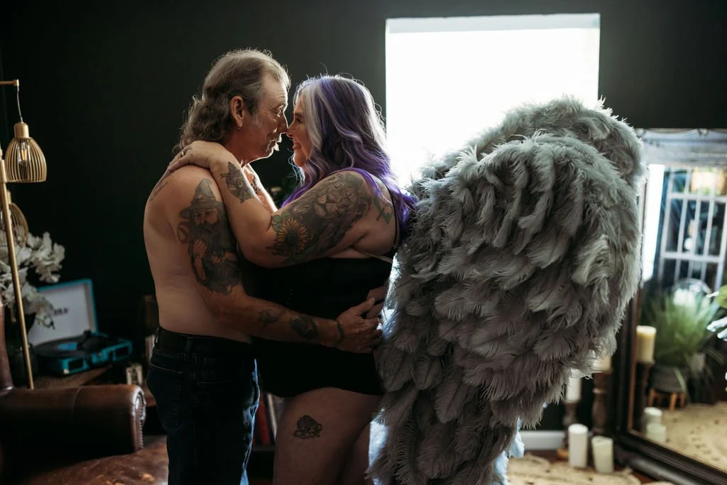 Older couple embracing and smiling at each other beside gray angel wings