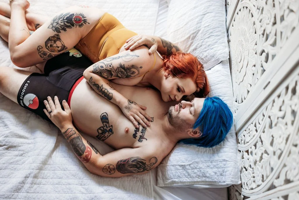 Tattooed couple looking at each other while posing together on a bed