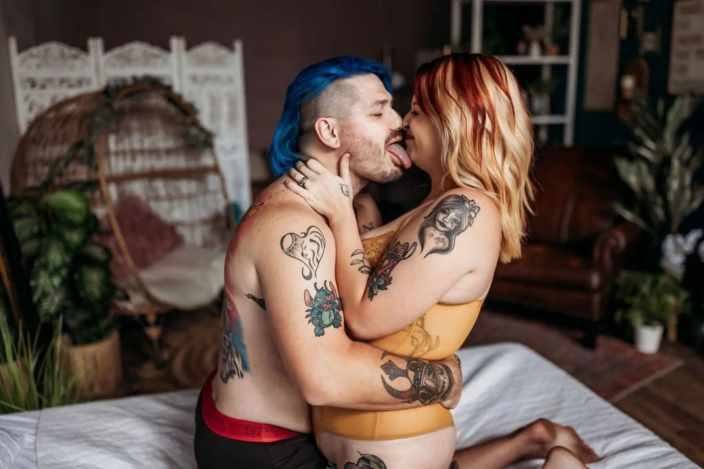 Tattooed couple playfully sticking out their tongues while posing together on a bed