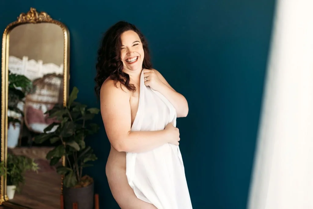 Woman laughing while wrapped in a white sheet during her boudoir session in Jacksonville