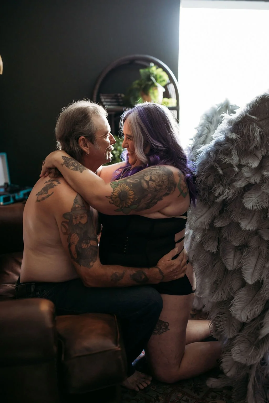 Older couple embracing beside gray angel wings during their Jacksonville couples boudoir session