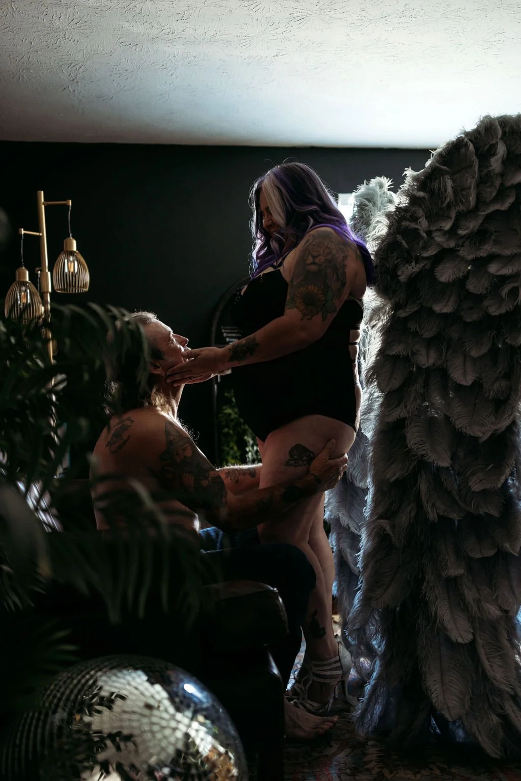 Tattooed couple posing intimately with gray angel wings during their couples boudoir session