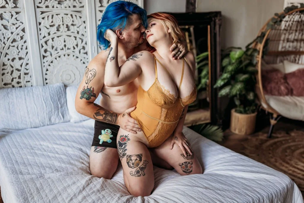 Tattooed couple posing closely together on a bed during their alternative boudoir session