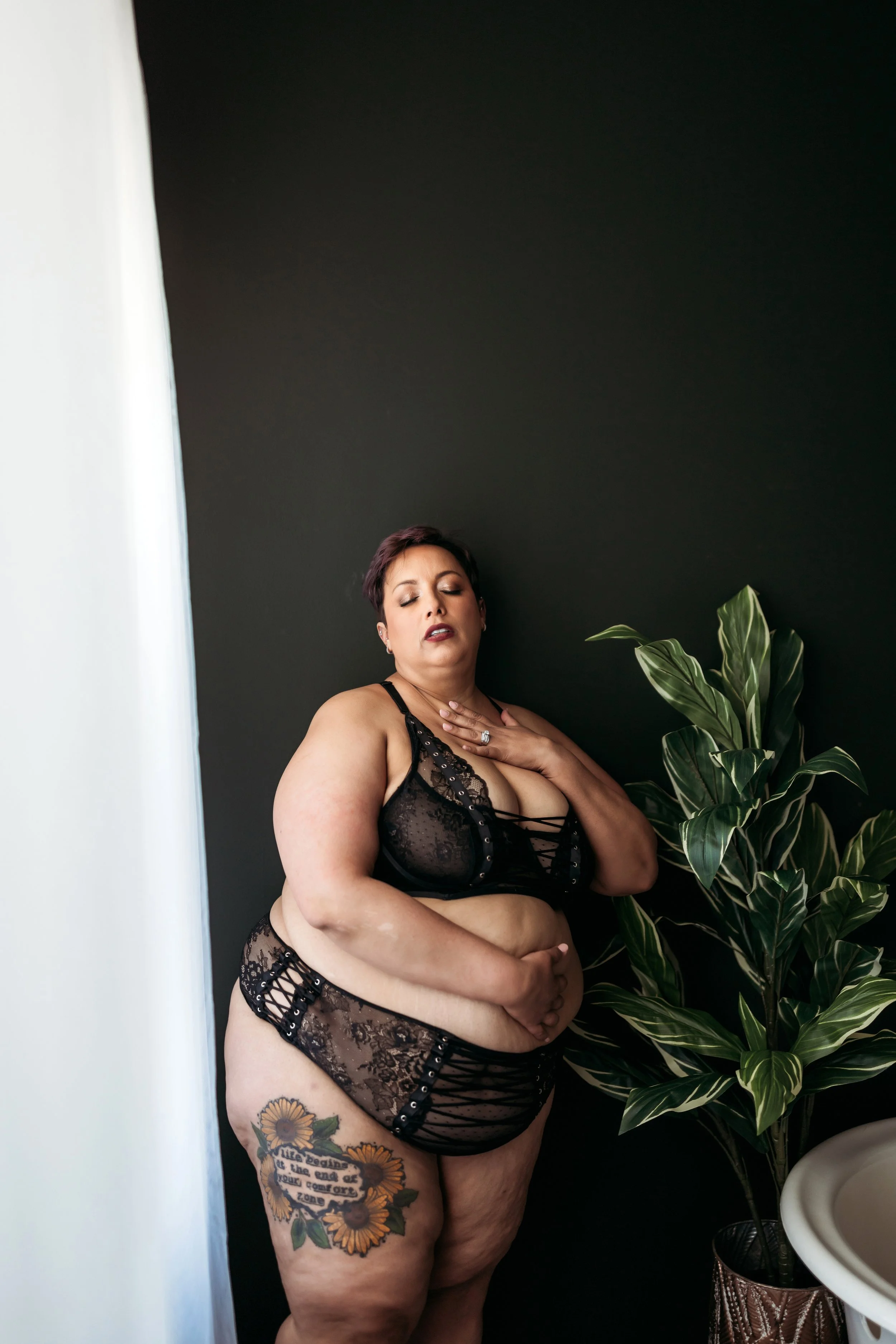 Plus-size woman posing in black lace lingerie beside plants during her Jacksonville boudoir session