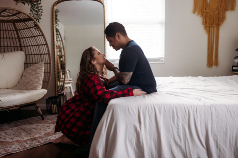 Couple sitting together on a bed, one wearing a red plaid shirt.