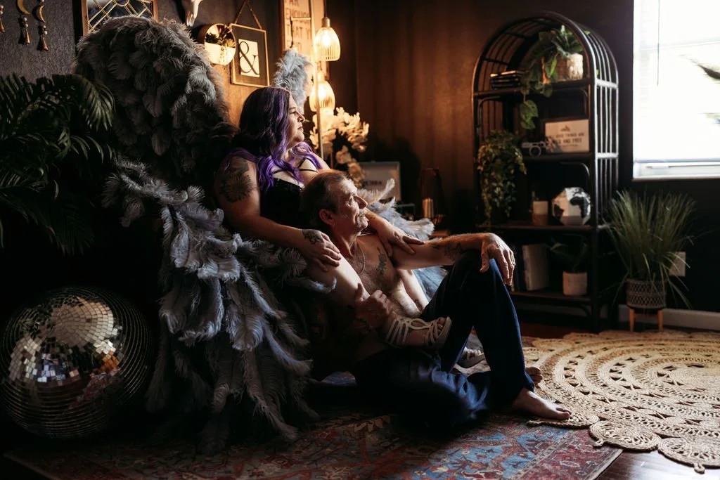 Older couple posing together with gray angel wings during a boudoir session in Jacksonville