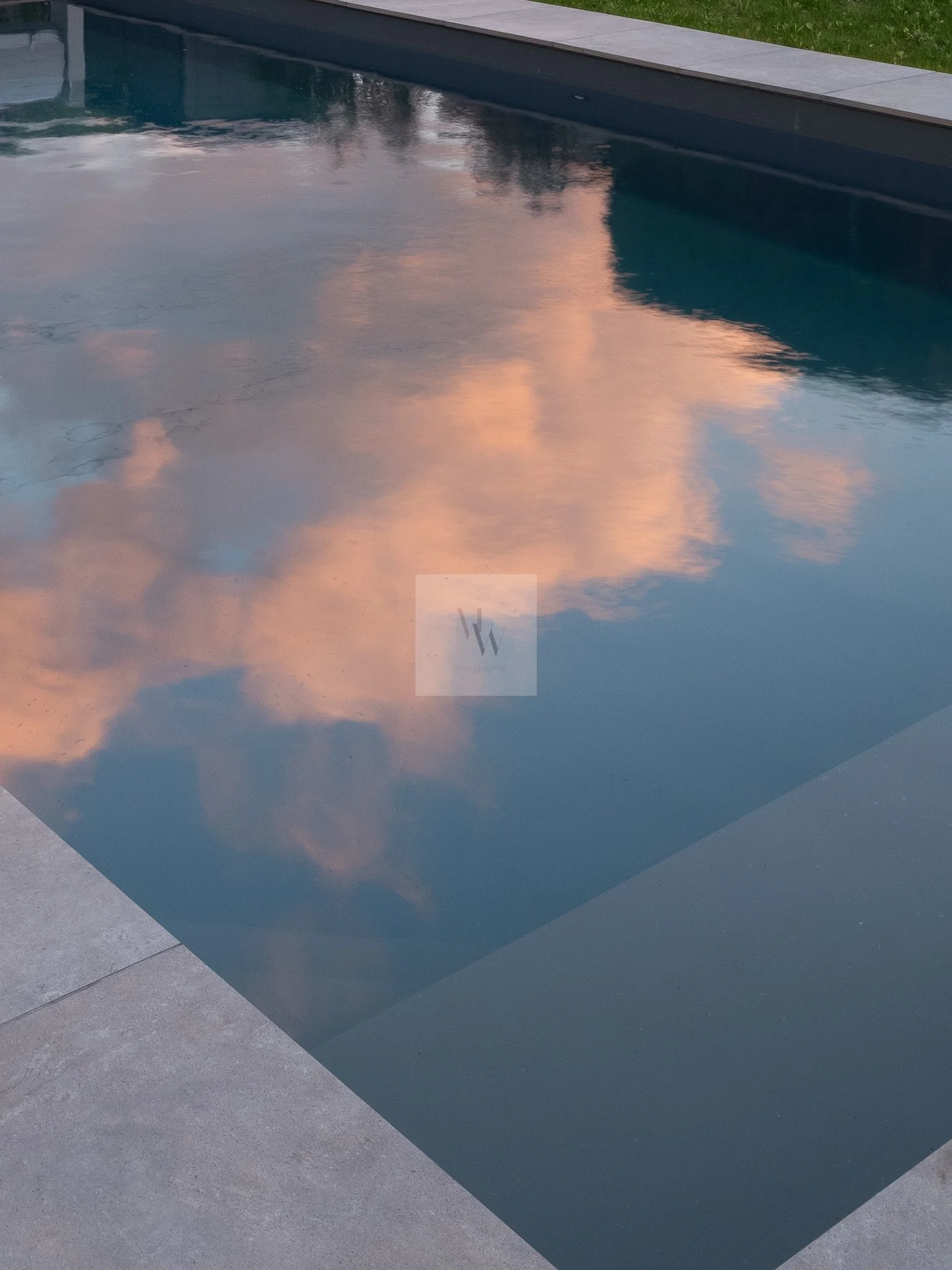 Reflet de nuages roses dans une piscine d'eau bleue entourée de margelles en pierre. Architecture