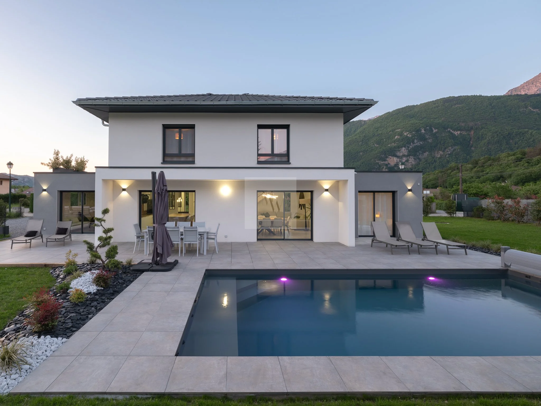 Maison moderne avec piscine, terrasse et chaise longues, située dans un paysage montagneux. Photographie immobilière premium pour locations saisonnières à Annecy