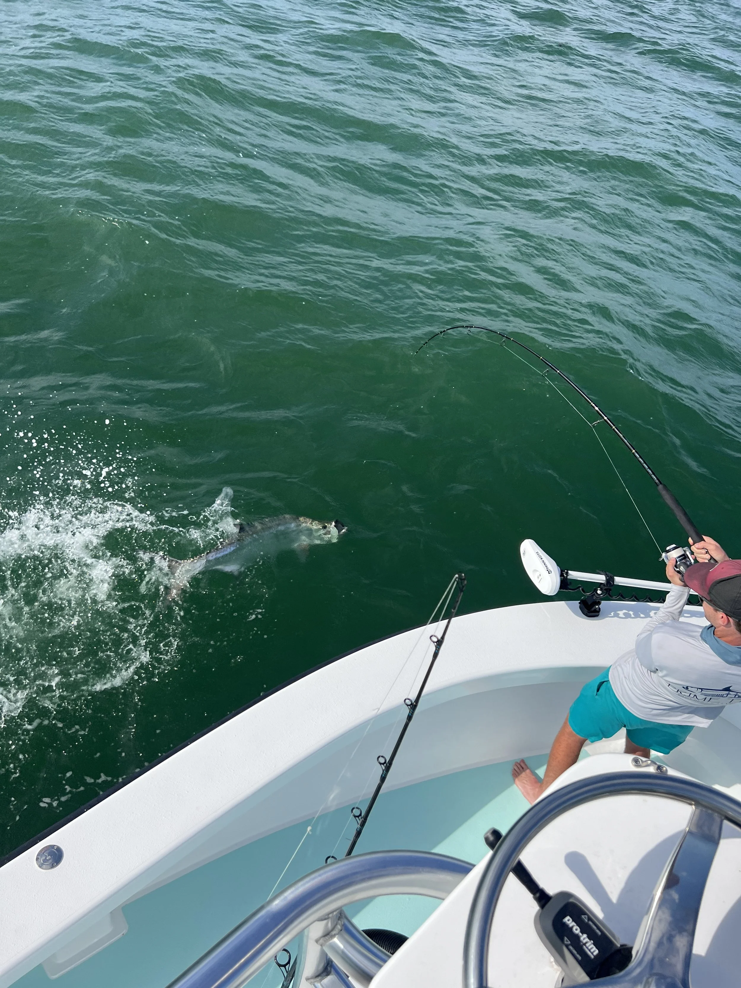 Fisherman on a boat reeling in a large fish in green water.