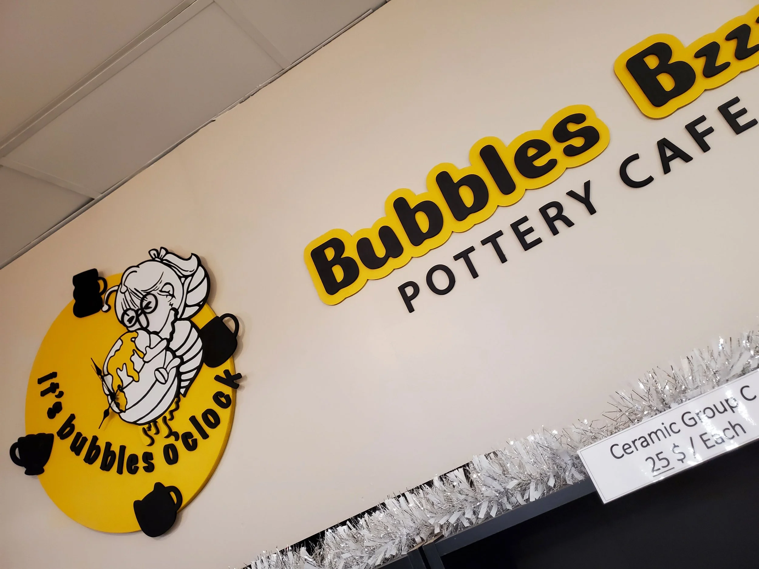 Laser-cut "Bubbles Bzzz" and "POTTERY CAFE" business sign. Includes a cartoon mascot of a bee with glasses, holding a honey comb on the custom-made clock with wooden 3D pottery elements.