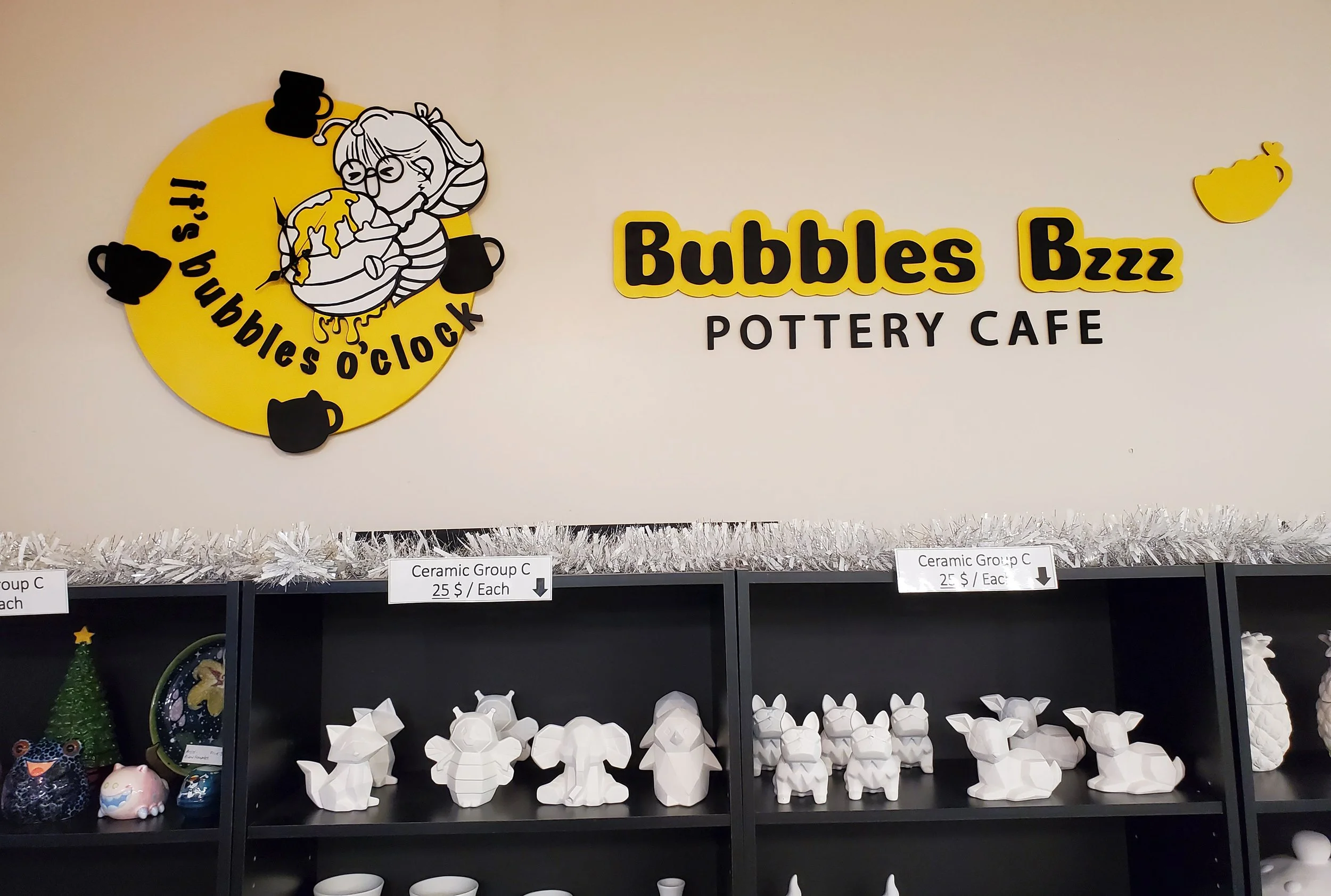 Display of ceramic pottery at a shop, with a laser-cut business sign and custom wooden clock for Bubbles Buzz Pottery Cafe.