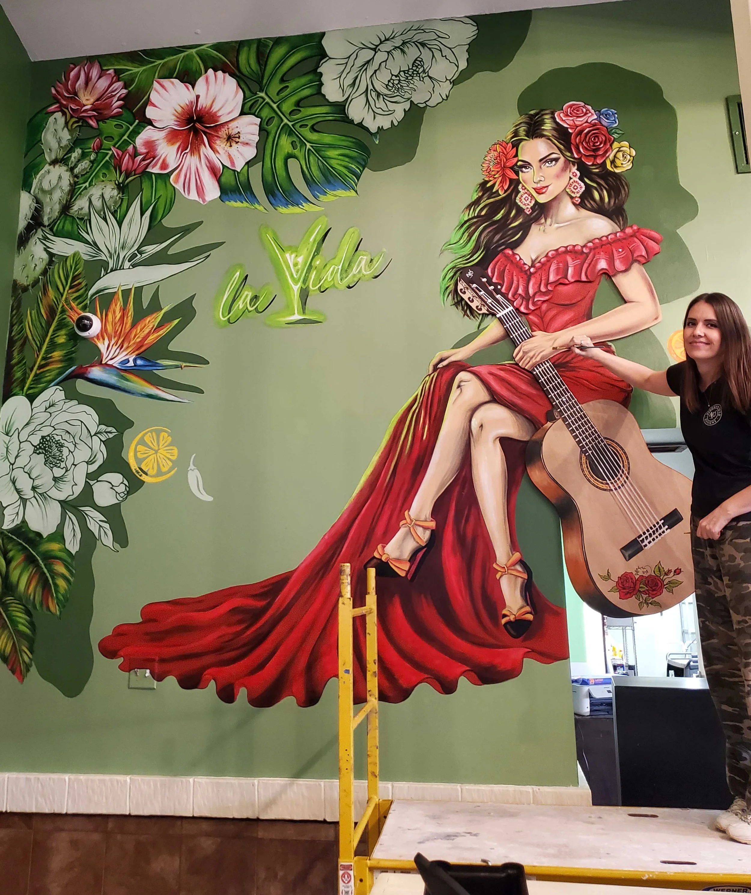 Veronika Neto next to custom guitar cut-out and mural of a woman in red dress