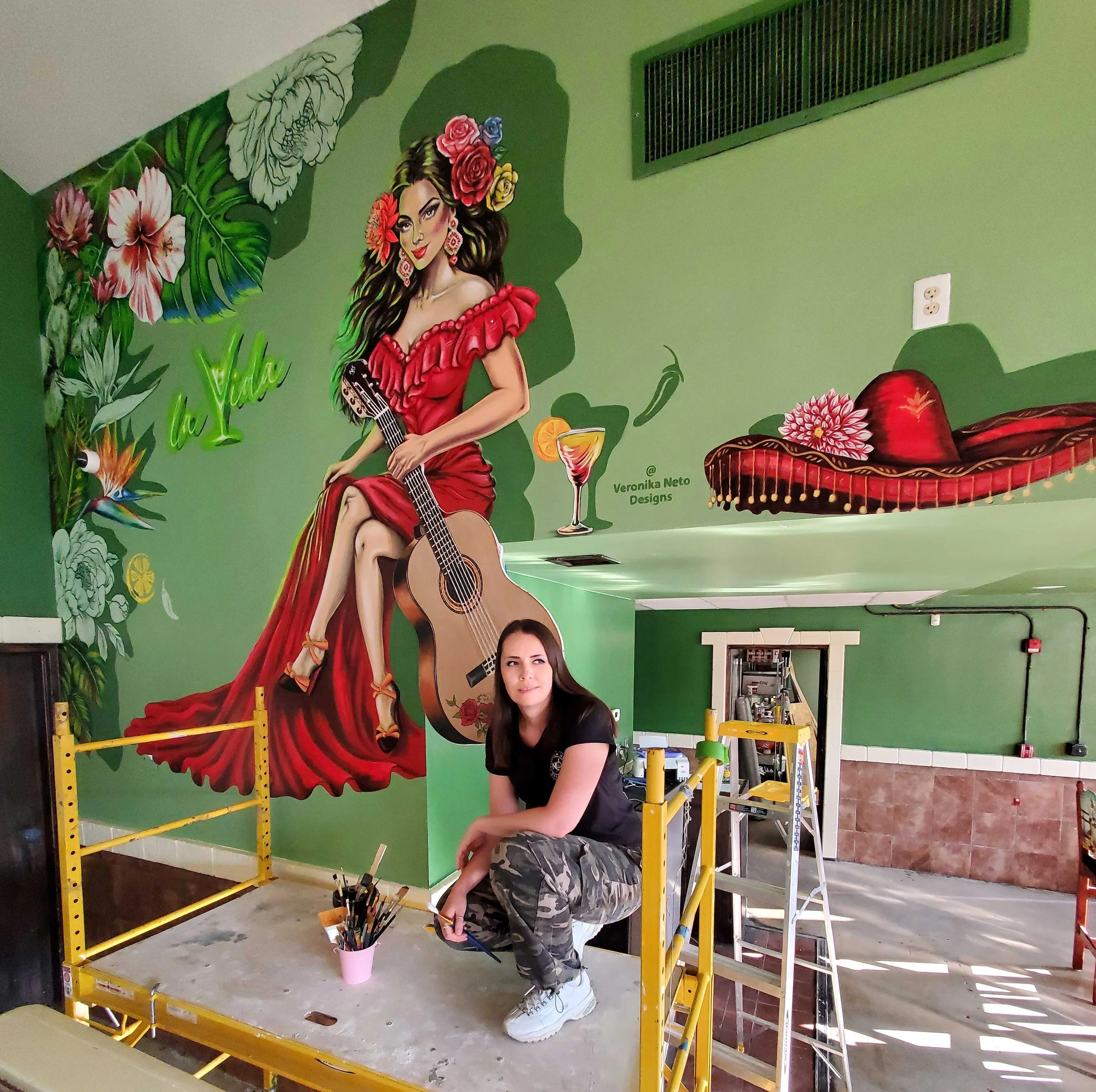 artist Veronika Neto with mural of a women in a red dress holding a custom cut and hand-painted  guitar