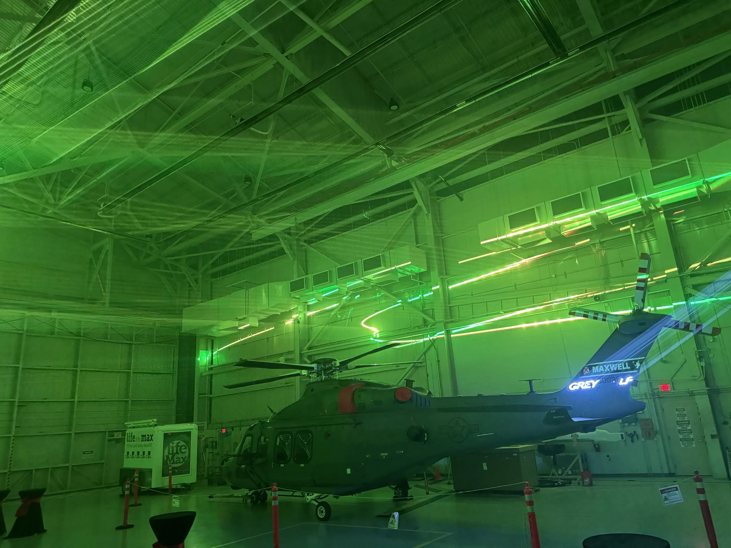 A military helicopter displayed indoors in a museum with green neon light reflections on the ceiling.