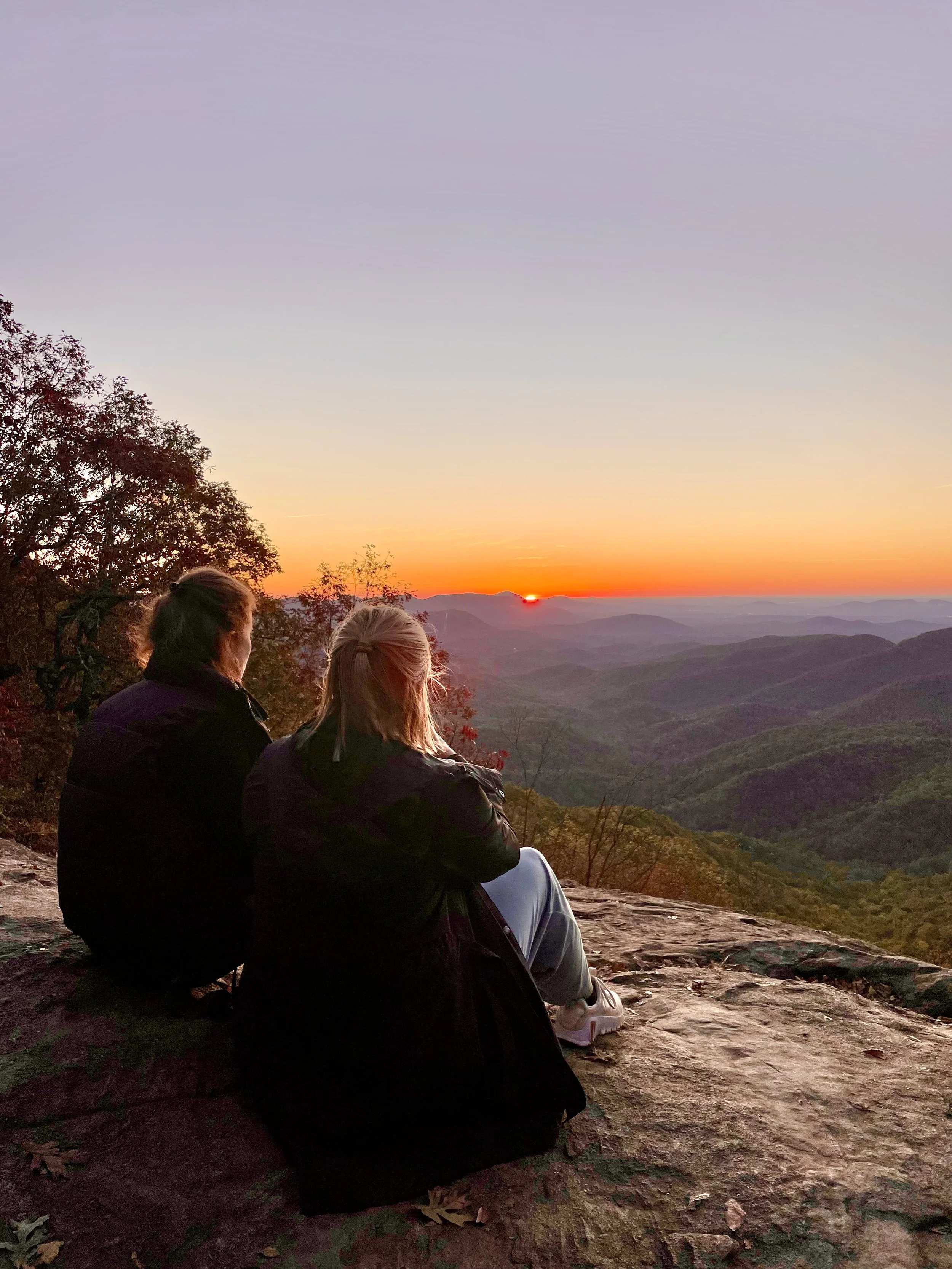 Photo of two women who took part in the Blue Ridge Business Retreat for Women in the fall of 2025. They're shown here on top of a mountain overlooking the sunrise at Preacher's Rock, where we enjoyed hot morning coffee after an invigorating hike.