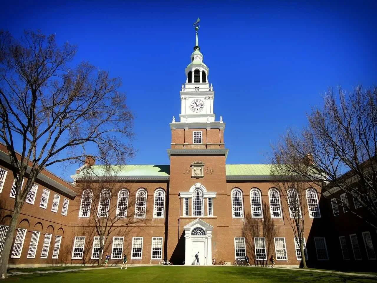 Dartmouth College Baker Library tower with brick academic building, students walking across the lawn, and clear blue sky
