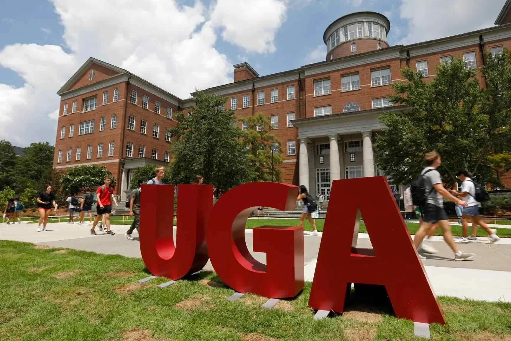 University of Georgia campus with large red UGA sign and students walking in front of a brick academic building