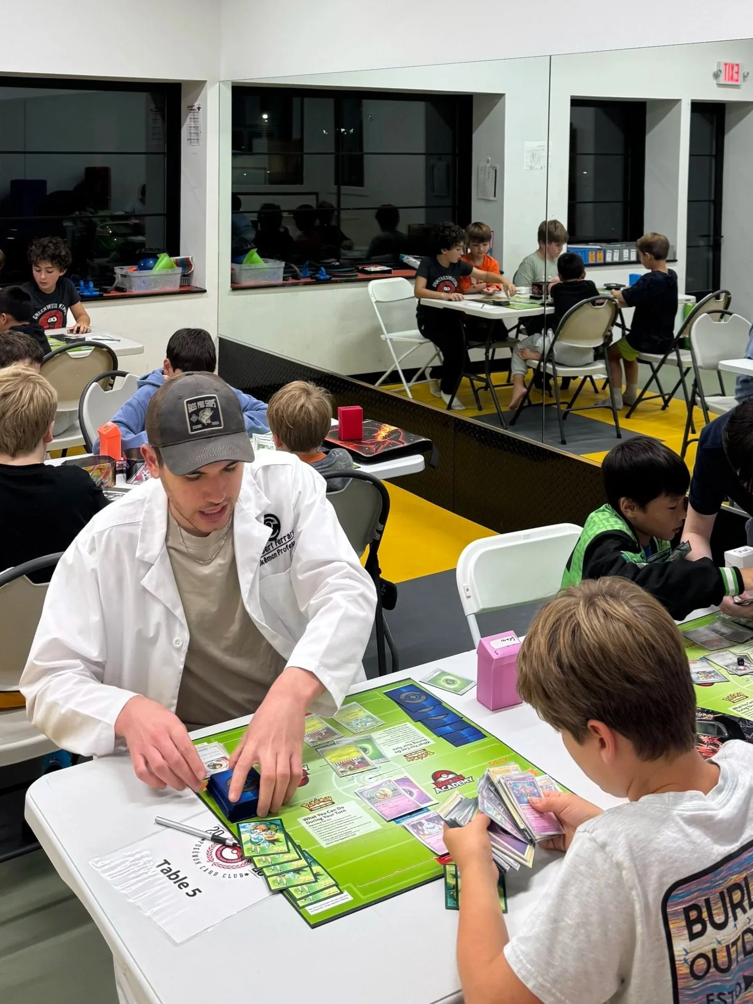 Children playing a trading card game at a table during a Pokémon tournament or event.