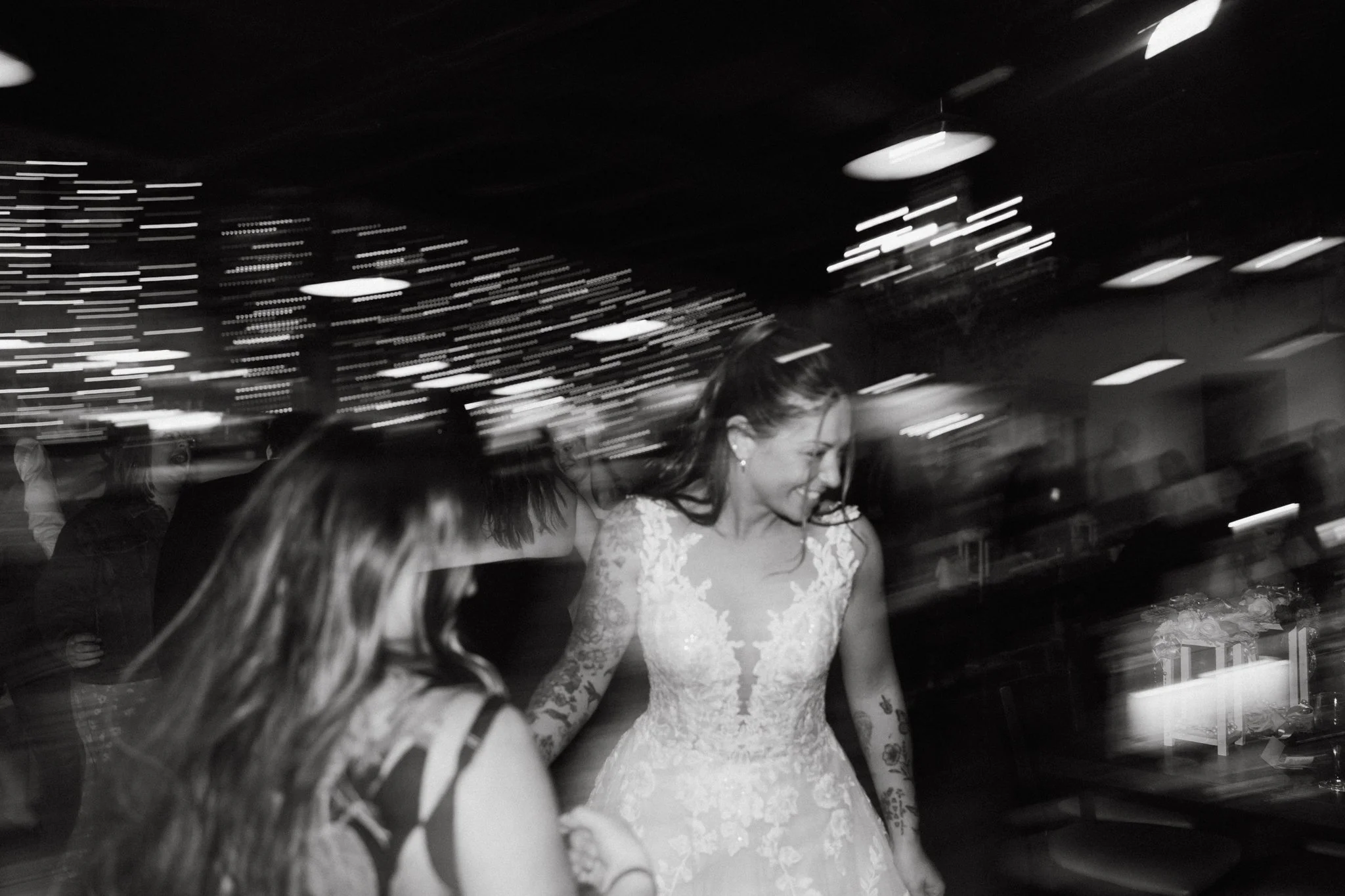 Black and white photo of two women dancing at a wedding reception, with blurred background and motion effects.