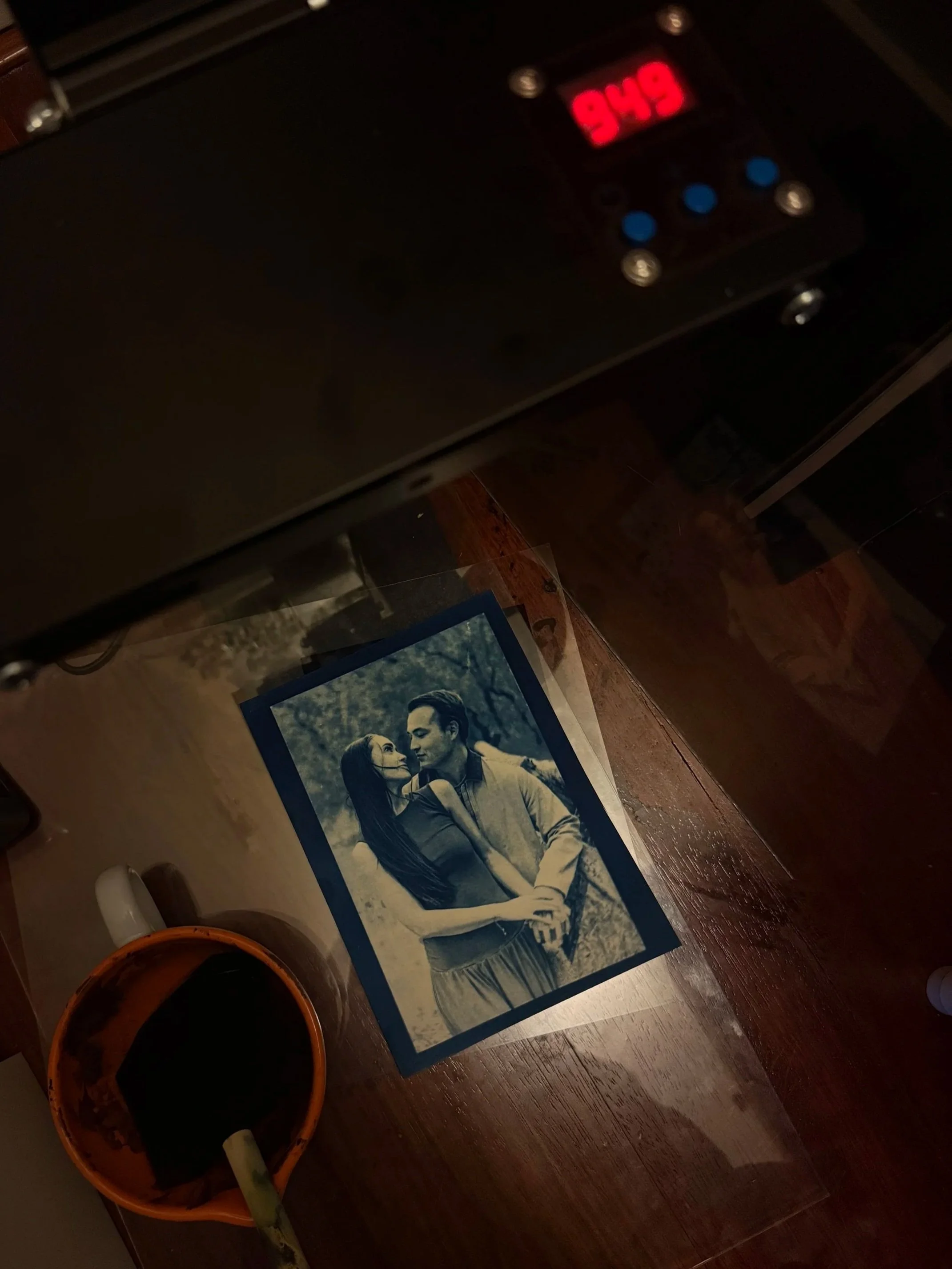 A black and white photograph of a loving couple standing outdoors, with the woman looking at the man and leaning in close, in a wooded area.