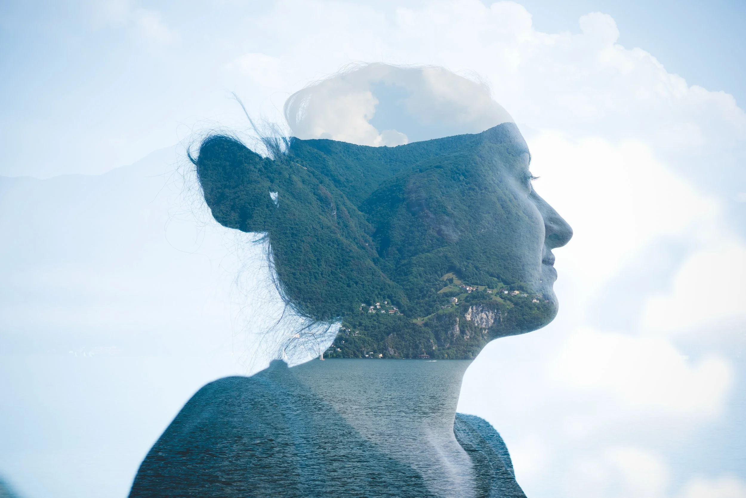 A double exposure photograph combining a woman's profile with a landscape of a mountain, trees, and water.